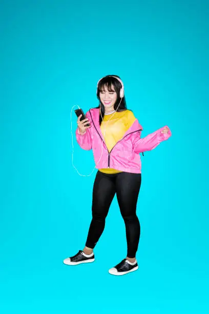 Portrait of attractive female dancer listening to music on a mobile phone with headphones in the studio
