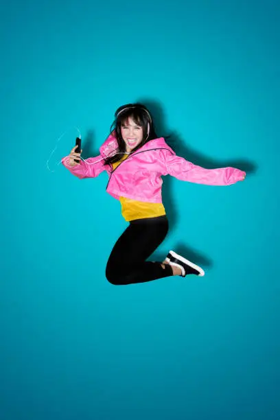 Joyful young woman listening to music with a mobile phone while jumping in the studio