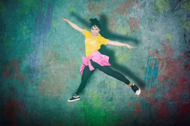 Young female hip-hop dancer jumping in the studio over a wall background