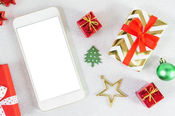 Close up mobile smartphone white screen with copy space for text Christmas New year theme red craft gift box ribbon bow with golden star on glitter background.