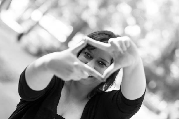 Young woman photographer framing a shot using her fingers Close up image of a young female caucasian photographer framing a shot using her fingers outdoors in the park. The focus is on her face which we can see through the frame she is making with her fingers. Horizontal black and white image with copy space. black and white portrait photographers stock pictures, royalty-free photos & images