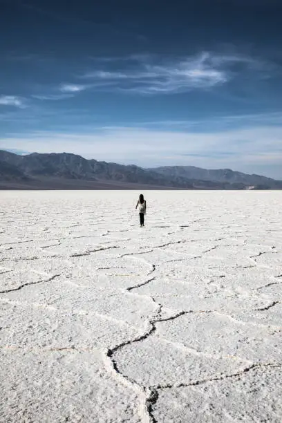 Mixed race woman walking alone in Badwater Basin salt flats in Death Valley, California. Heat of the day midday, hot weather. Lowest point in North America. Line of salt formations in foreground