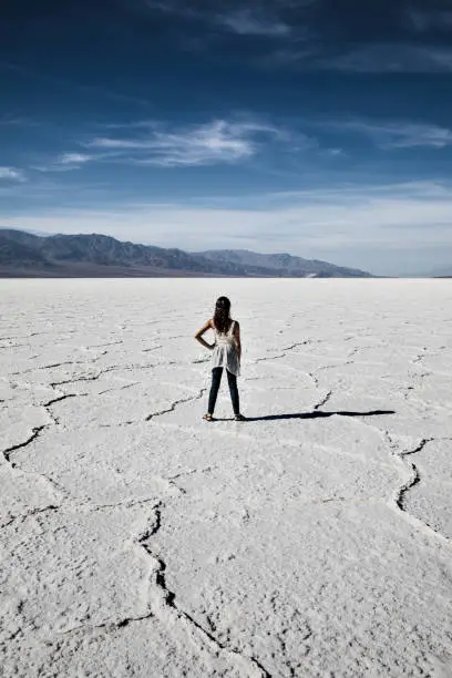 Beautiful mixed race woman standing alone in Badwater Basin salt flats in Death Valley, California. Shadow casted to the right of her. Heat of the day midday, hot weather. Lowest point in North America