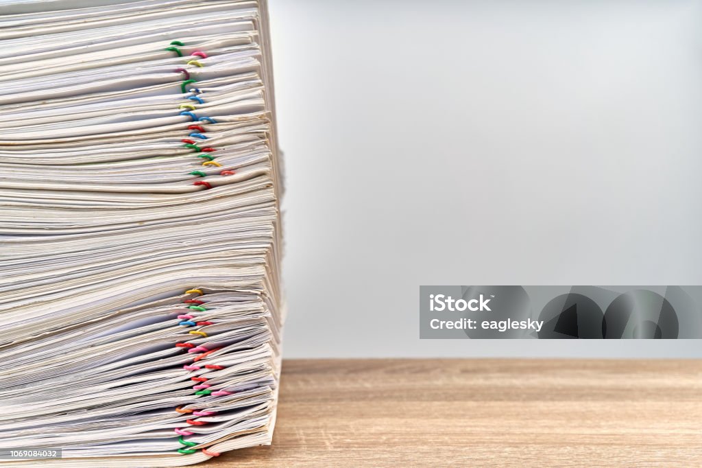 Pile overload paperwork report on wooden table with copy space Pile of overload paperwork report of sale with colorful paper clip on wooden table with white background and copy space. Stack document is high as work hard. Business and finance concept success. Paper Stock Photo