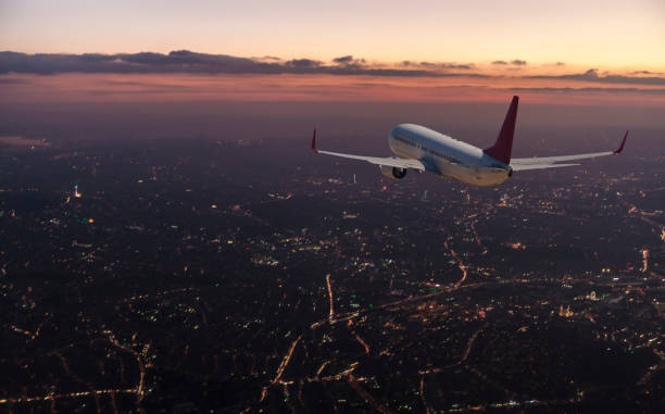 Commercial airplane flying over big city at dusk Commercial airplane flying over big city at dusk airplane stock pictures, royalty-free photos & images