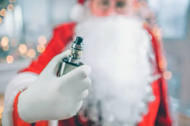 Close up of Santa Claus stands and holds vape in hand. He shows it on camera