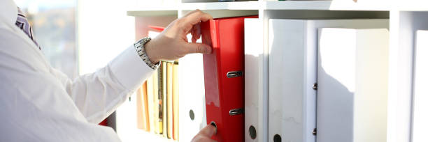 istock Male arms pick red file folder from office book shelf 1069114450