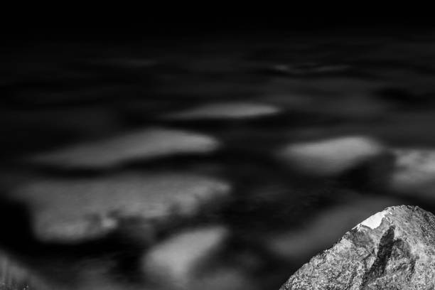 Black and white, monochrome, abstract, background, composition of stones submerged in water, stone with visible rugged texture, space and water surface . Blackness and atmosphere of serenity in rocky landscape. Rocks detail, close-up.