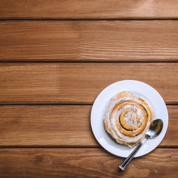 istock Cinnamon bun on a white plate on a dark wooden background. Top view, copy space, flat lay 1069137144