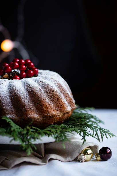 istock Holiday table with a Christmas cake decorated with red cranberries and pine cones on white table and dark background. 1069146228