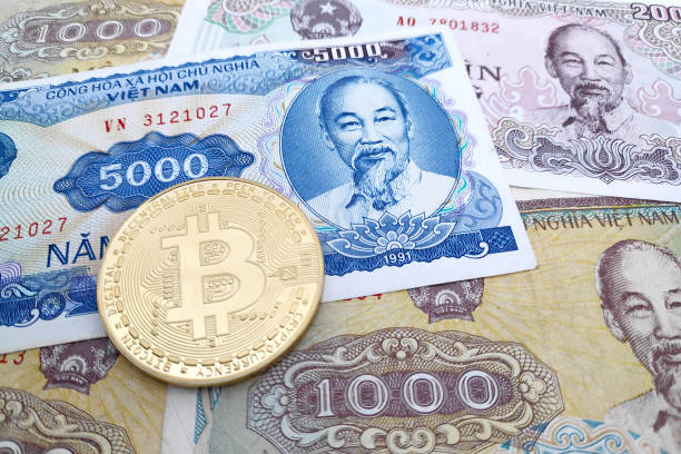 Bitcoin coin on top of a stack of Vietnamese Dong banknotes Close-up on a golden Bitcoin coin on top of a stack of Vietnamese Dong banknotes. dong stock pictures, royalty-free photos & images