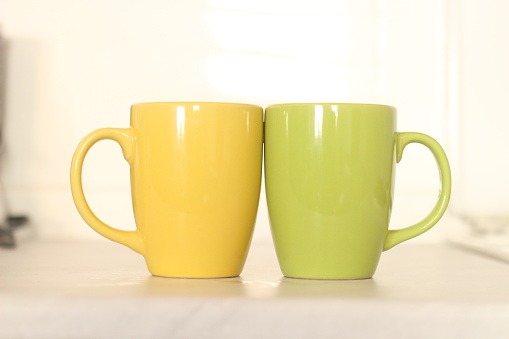 Side view on a green and yellow coffee mug with hot coffee on table in domestic room