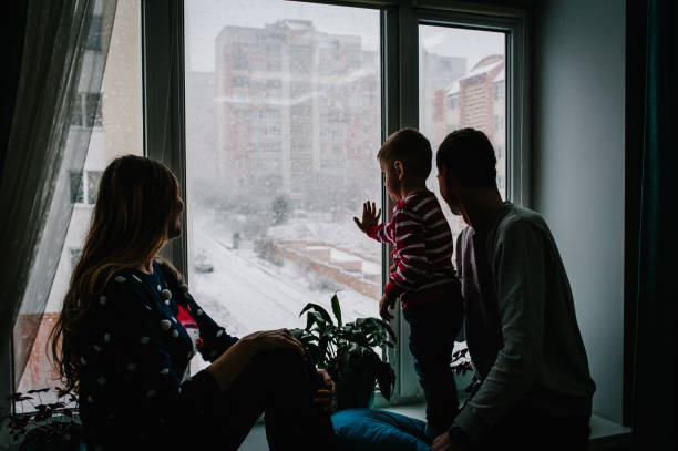 merry christmas and happy holidays! happy family: mom, dad and little son in santa claus sweaters sitting on window and looking at the winter park. room decorated on christmas. enjoy the snowfall. - window christmas night house imagens e fotografias de stock