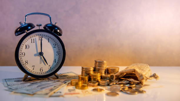 istock Clock with banknotes and coin stack of international currency on table. Time investment or retirement saving. Business and finance concepts 1069154352