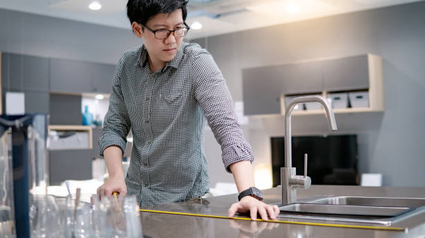 istock Young Asian man using tape measure for measuring granite countertops on modern kitchen counter in showroom. Shopping furniture for home improvement. Interior design concept 1069155702