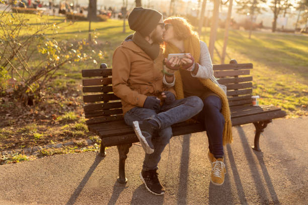 Young couple kissing on the park bench at golden hour on a sunny winter day.