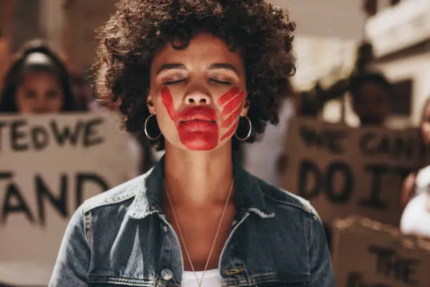 Woman with a hand print on her mouth, demonstrating violence on women. Woman protesting against domestic violence with group in background.