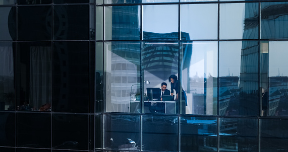 Aerial Shot From Outside of the Skyscraper: Businessman and Businesswoman Talking Business while Sitting at the Desk by the Office Window. Shot of the Financial District and Businesspeople Working in the Big City.