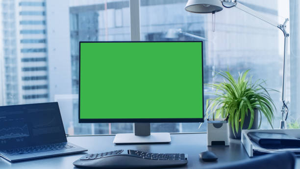 istock Shot of the Office Desk with Green Mock-up Screen Personal Computer Standing on it. Modern Stylish Room with a Big City Business District View. 1069159852