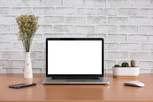 Blank screen of laptop computer with dry flowers, iPhone X and cactus vase on white bricks background