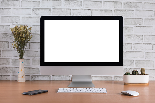 Blank screen of all in one computer with dry flowers, iPhone X and cactus vase on white bricks background