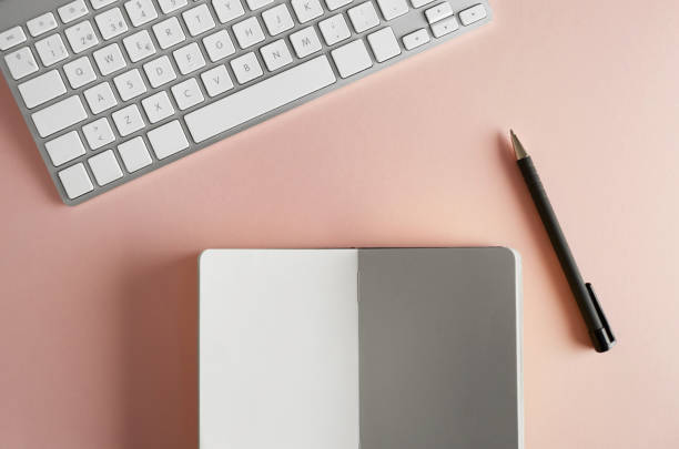 istock Mockup of paper note book, computer keyboard on empty color desk. Business empty mock-up background for message writing.Top view. 1069163938