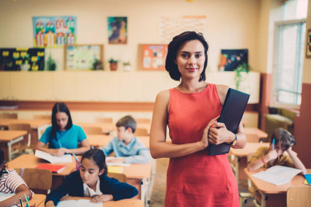 Schoolchildren studying in class and teacher looking at camera