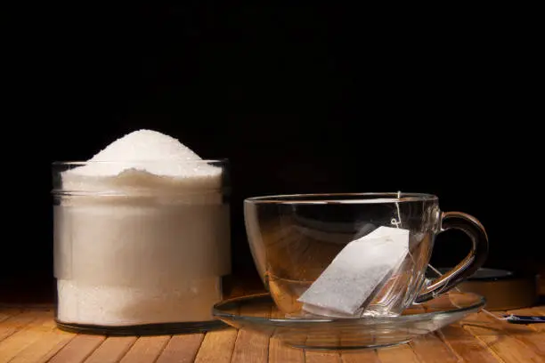 A cup of tea teabag and sugar bowl.