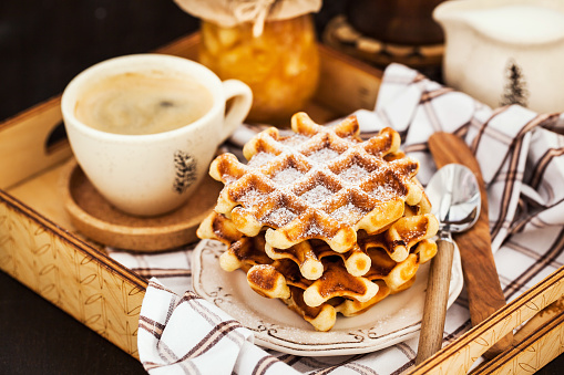 Breakfast with belgian waffles, jam and coffee on tray, rustic background