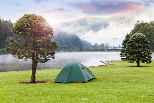 Camping near apline mountain lake. Tent on the green grass lawn