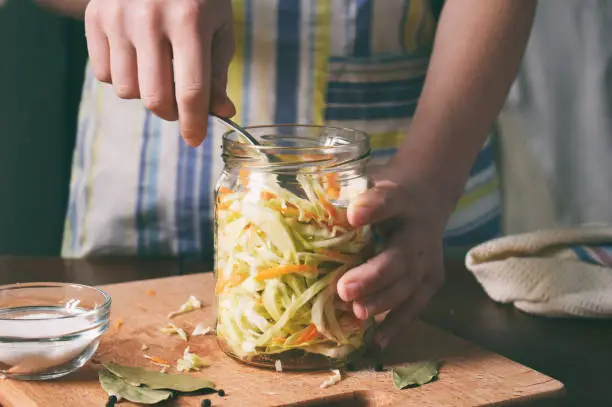 Woman cook sauerkraut or salad on wooden background. Step 5 - Put the cabbage in the jars. Fermented preserved vegetables food concept