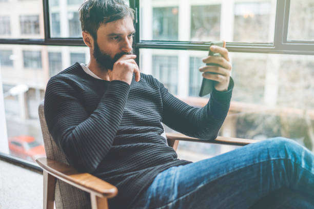 istock Young cute bearded man sitting home and using smartphone for surfing web internet. Man using gadget at modern apartment. Horizontal. Blurred background. 1069173058