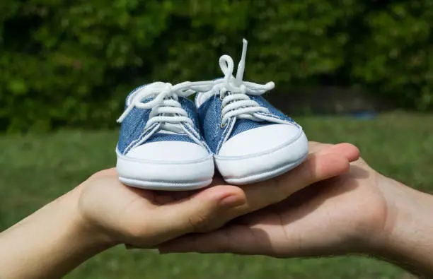 Young future parents holding baby shoes outdoors