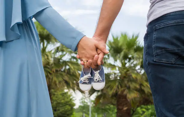 Future parents holding hands and baby shoes while walking outdoors