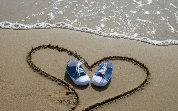 Baby shoes on the beach in heart shape