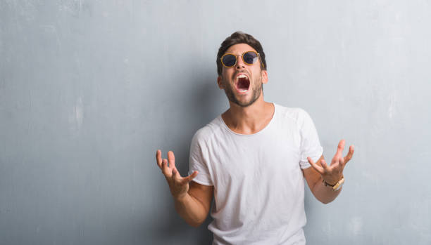 istock Handsome young man over grey grunge wall wearing sunglasses crazy and mad shouting and yelling with aggressive expression and arms raised. Frustration concept. 1069183498