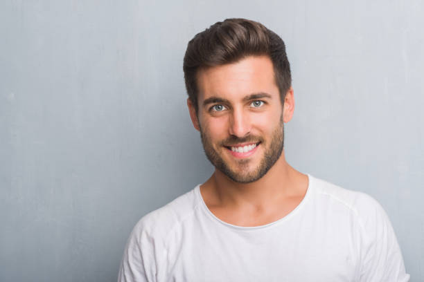 Handsome young man over grey grunge wall with a happy face standing and smiling with a confident smile showing teeth