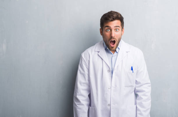 istock Handsome young professional man over grey grunge wall wearing white coat afraid and shocked with surprise expression, fear and excited face. 1069184902
