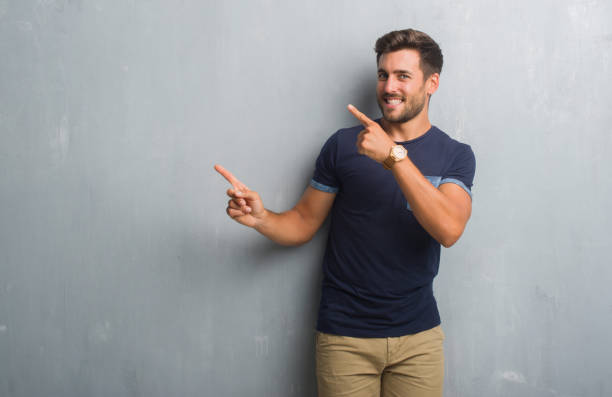 istock Handsome young man over grey grunge wall smiling and looking at the camera pointing with two hands and fingers to the side. 1069185270