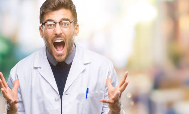 istock Young handsome man wearing doctor, scientis coat over isolated background crazy and mad shouting and yelling with aggressive expression and arms raised. Frustration concept. 1069186310