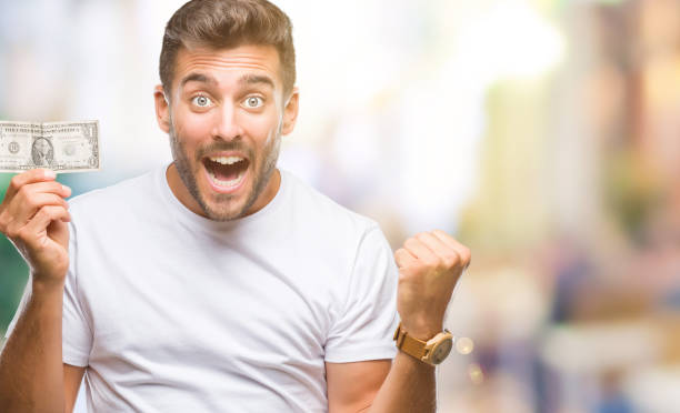 istock Young handsome man holding dollars over isolated background screaming proud and celebrating victory and success very excited, cheering emotion 1069187874