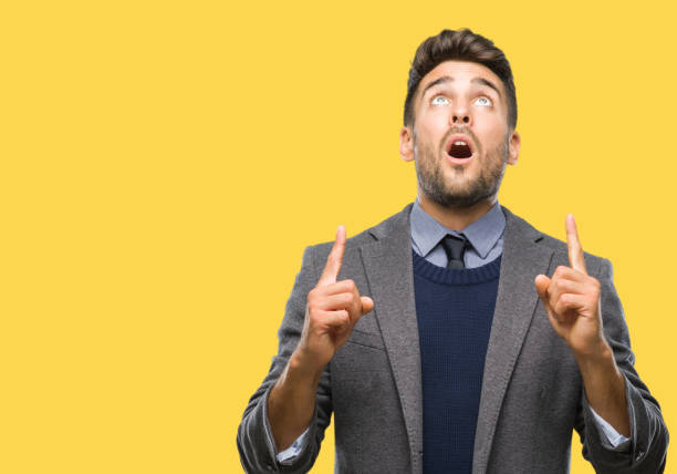 istock Young handsome business man over isolated background amazed and surprised looking up and pointing with fingers and raised arms. 1069188104