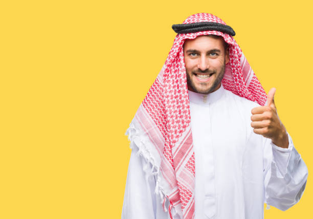 istock Young handsome man wearing keffiyeh over isolated background doing happy thumbs up gesture with hand. Approving expression looking at the camera with showing success. 1069188400