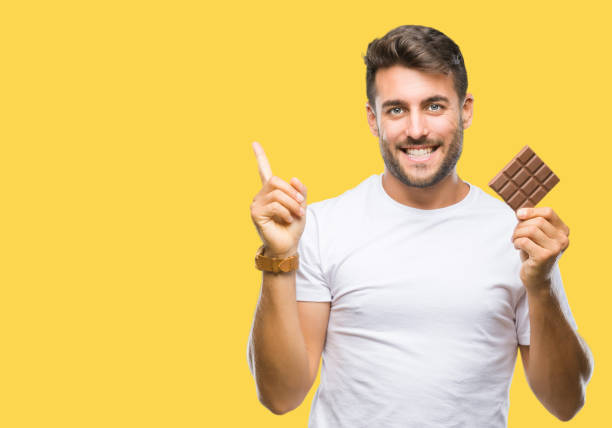 istock Young handsome man eating chocolate bar over isolated background very happy pointing with hand and finger to the side 1069188506