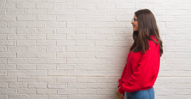 istock Young brunette woman standing over white brick wall looking to side, relax profile pose with natural face with confident smile. 1069192380