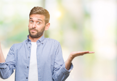 Young handsome man wearing white t-shirt over isolated background clueless and confused expression with arms and hands raised. Doubt concept.