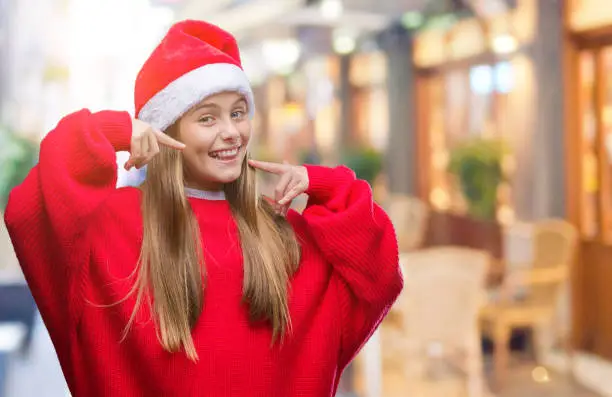 Photo of Young beautiful girl wearing christmas hat over isolated background smiling confident showing and pointing with fingers teeth and mouth. Health concept.