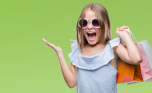 Young beautiful girl holding shopping bags on sales over isolated background very happy and excited, winner expression celebrating victory screaming with big smile and raised hands