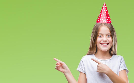 Young beautiful girl wearing birthday cap over isolated background smiling and looking at the camera pointing with two hands and fingers to the side.