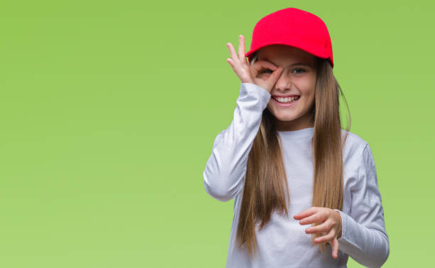 istock Young beautiful girl wearing red cap isolated background doing ok gesture with hand smiling, eye looking through fingers with happy face. 1069204176